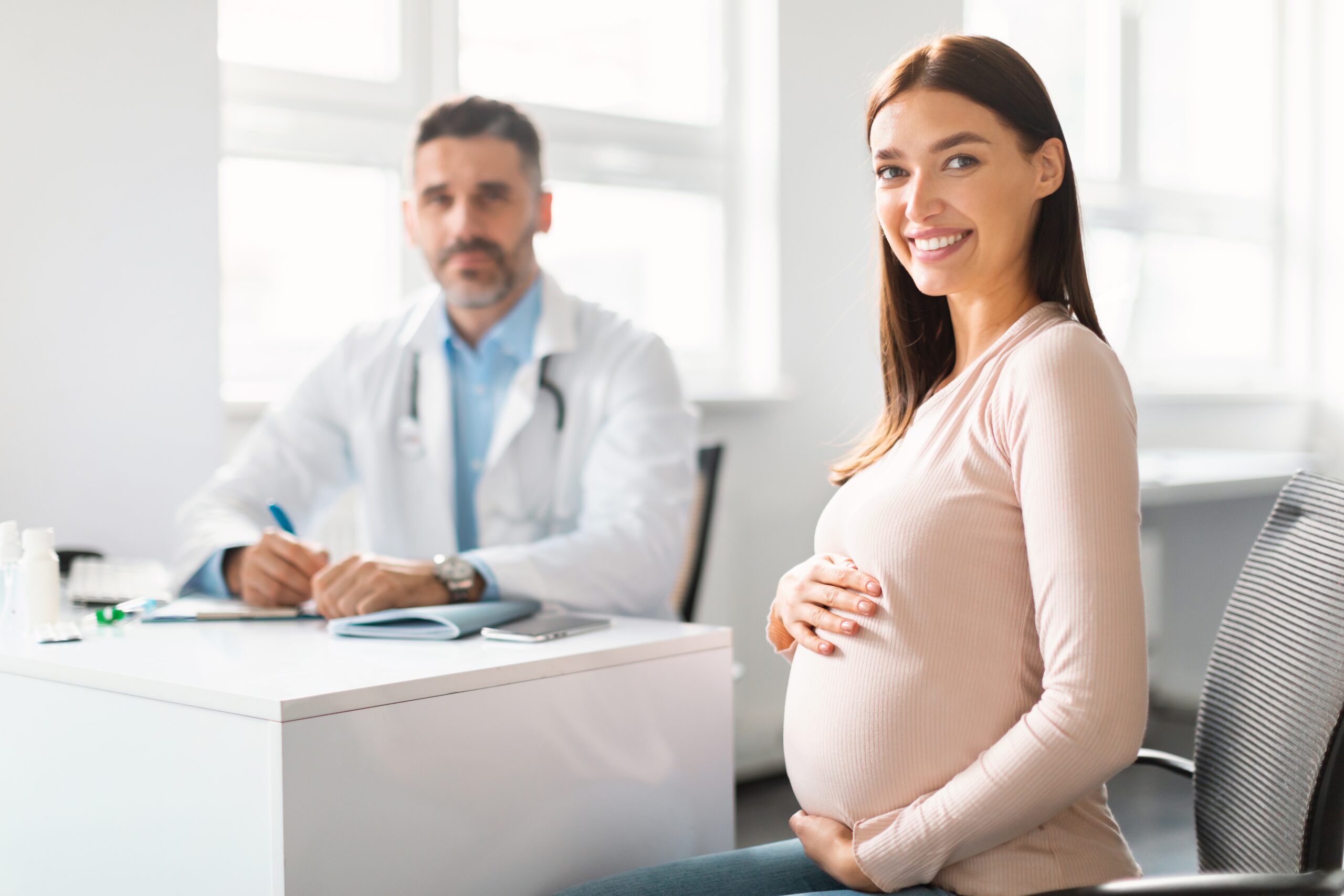 Mulher branca grávida em consulta com médico branco, possivelmente especialista em obstetrícia.