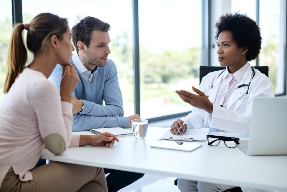 Profissional médica conversando com casal de pacientes.